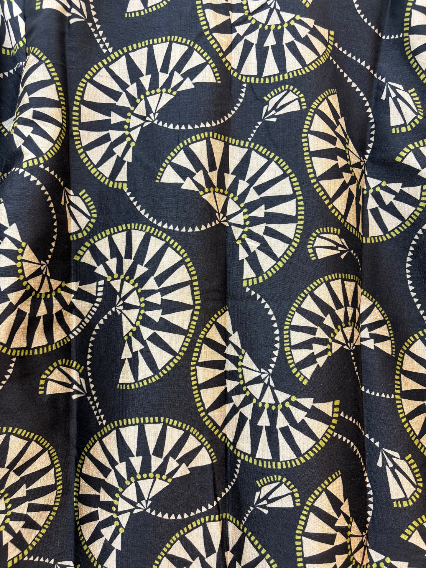 A close-up of a patterned fabric featuring a repeating geometric design of semi-circles and triangles in cream, black, and olive green on a dark navy background.