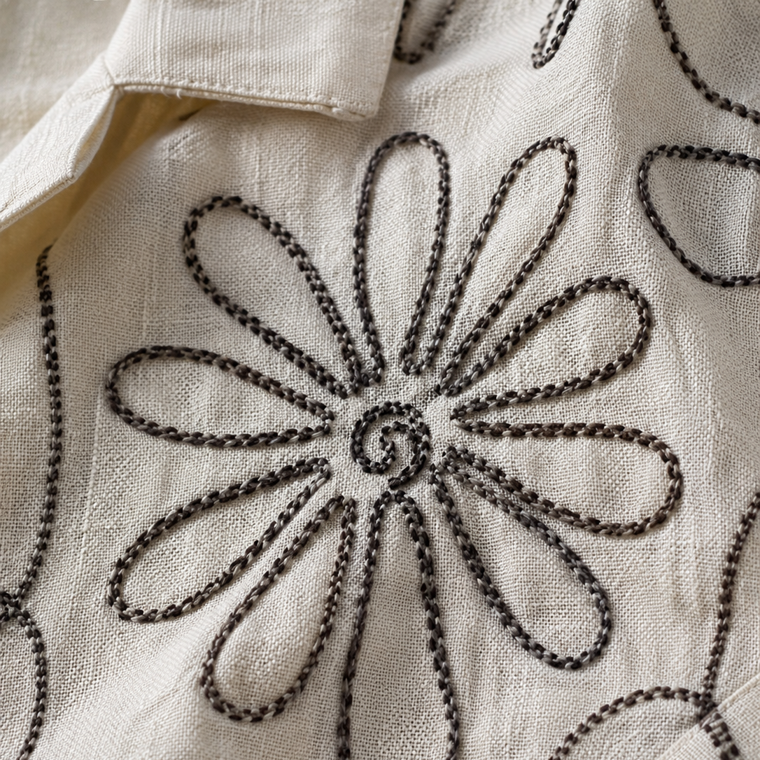 Close-up of an off-white textured fabric with dark brown embroidered floral outlines.